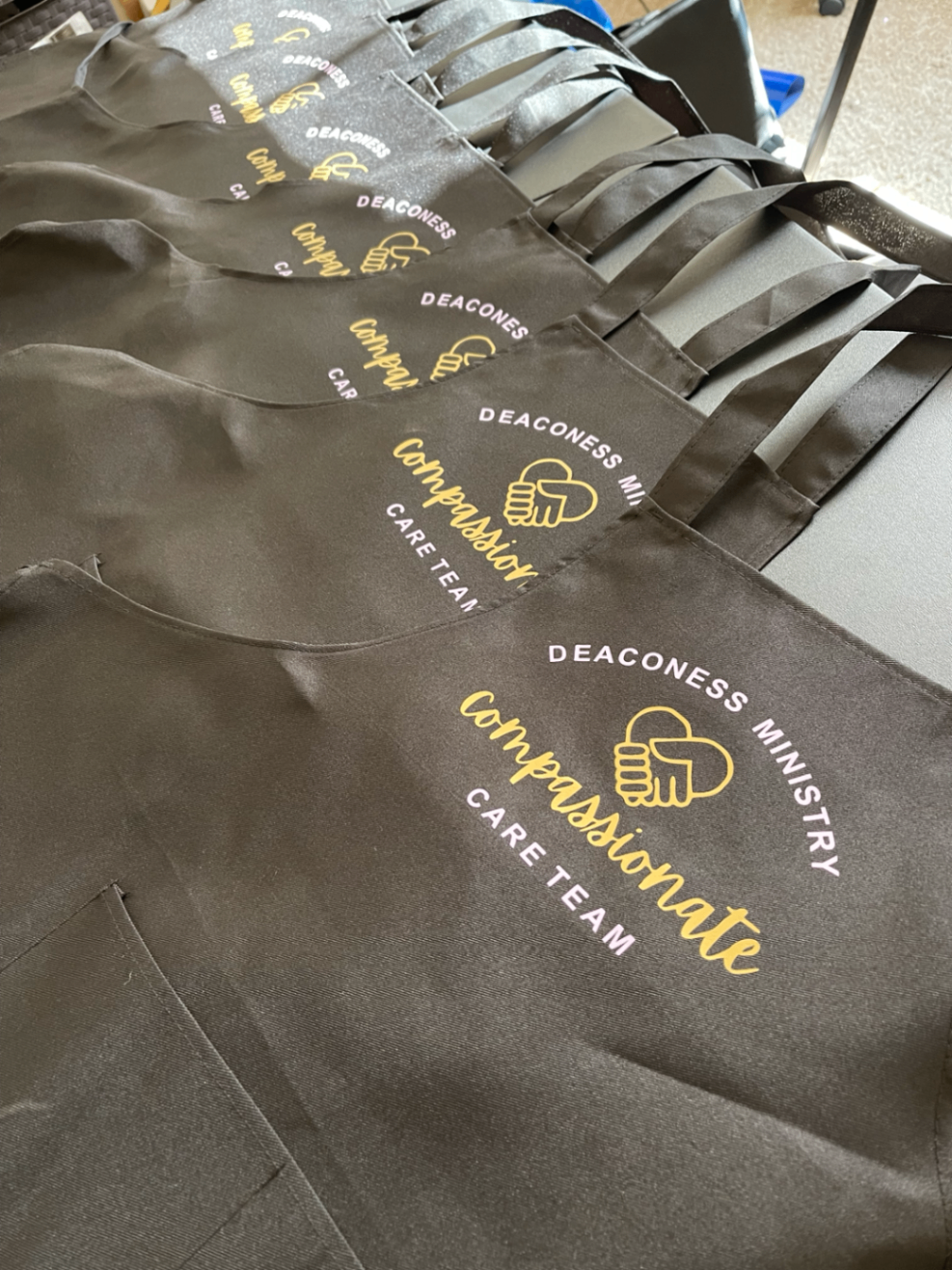Charcoal ministry aprons printed with gold Compassionate Care Team lettering